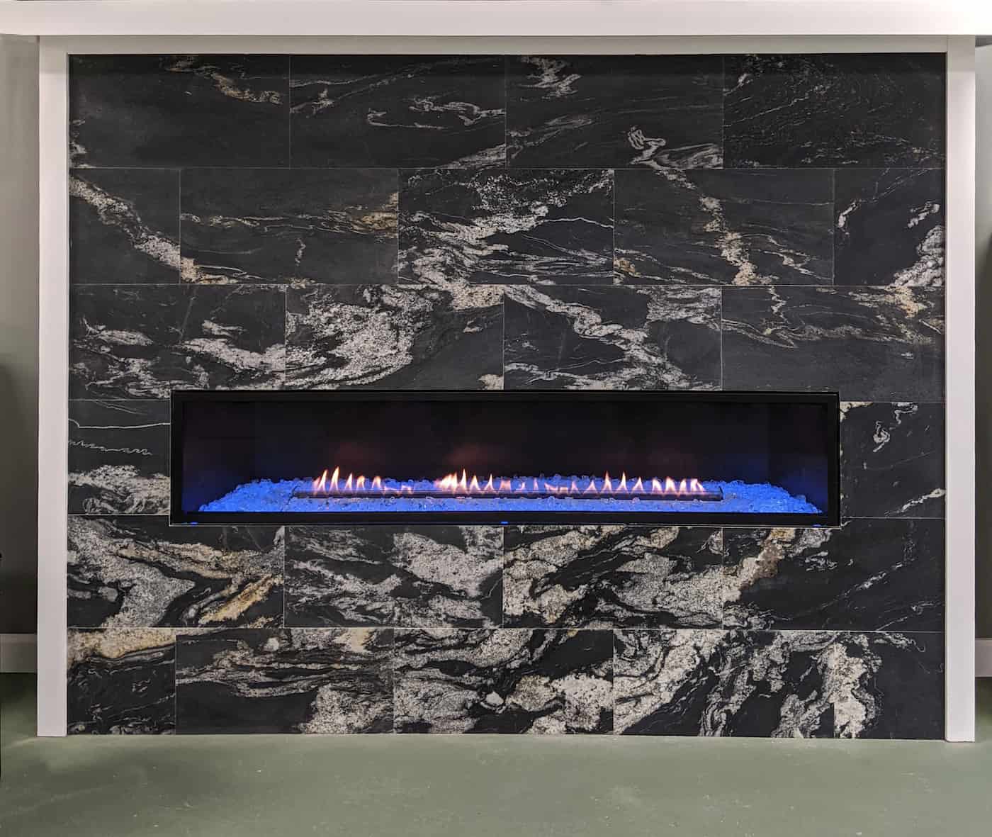 Black natural stone tile on a modern fireplace with a long gas insert and simple wood mantle. Each uniquely veigned honed granite tile provides a beautiful surface to the project.