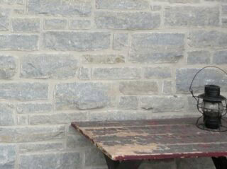 Tumbled finish loose limestone samples in shades of light grey, gold and blue-grey undertones set up on a wall of a home